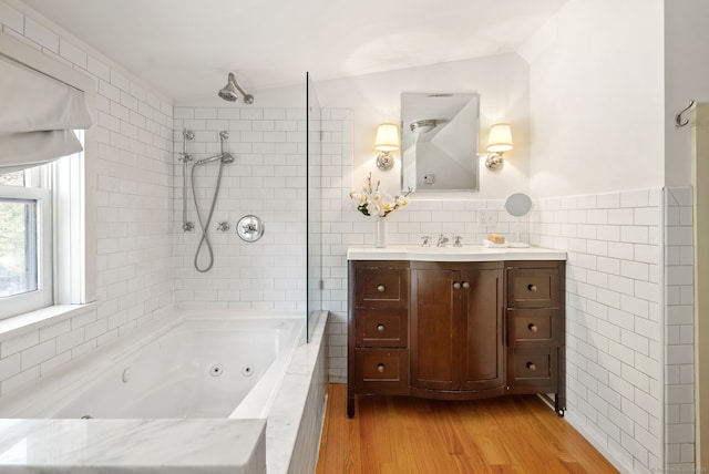 bathroom featuring hardwood / wood-style flooring, vanity, tiled shower / bath combo, and tile walls