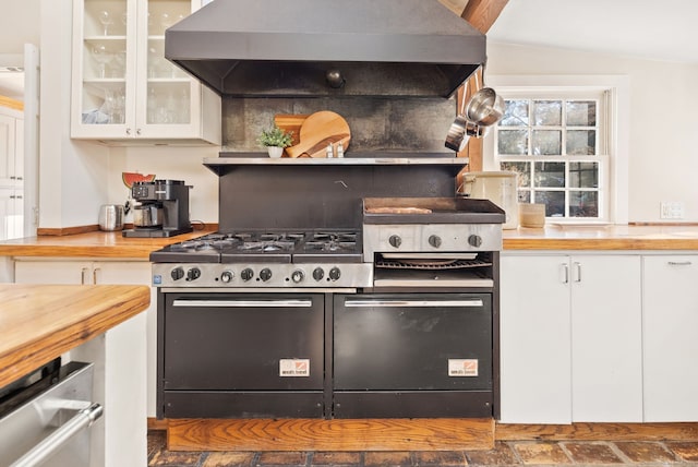 kitchen featuring vaulted ceiling, butcher block countertops, range with gas cooktop, white cabinets, and wall chimney exhaust hood