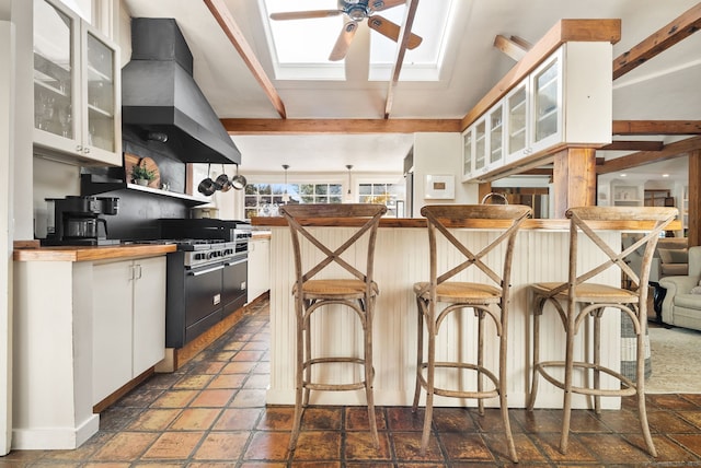 kitchen with butcher block countertops, double oven range, white cabinets, a kitchen bar, and custom exhaust hood