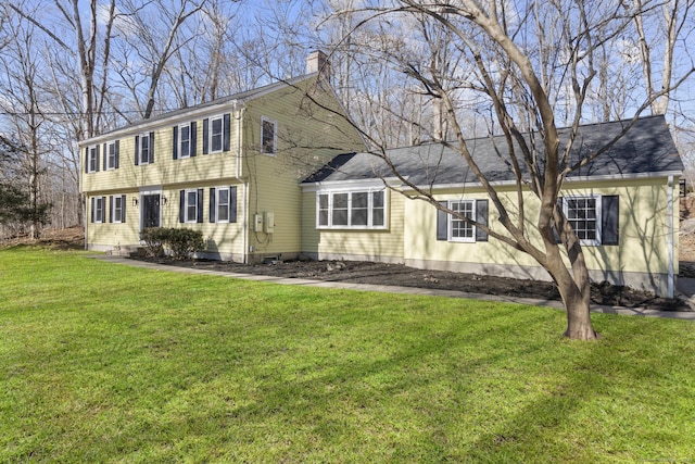 colonial-style house featuring roof with shingles, a front lawn, and a chimney