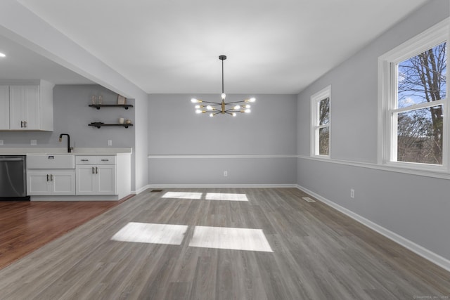 unfurnished dining area with wood finished floors, an inviting chandelier, a sink, and baseboards