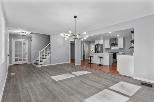 unfurnished living room with wood finished floors, visible vents, baseboards, stairs, and an inviting chandelier