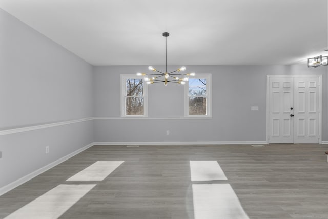 unfurnished dining area with a notable chandelier, baseboards, and wood finished floors