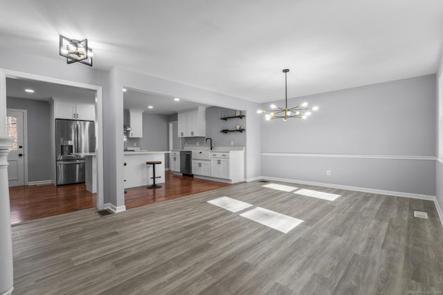 unfurnished living room with a sink, an inviting chandelier, wood finished floors, and baseboards