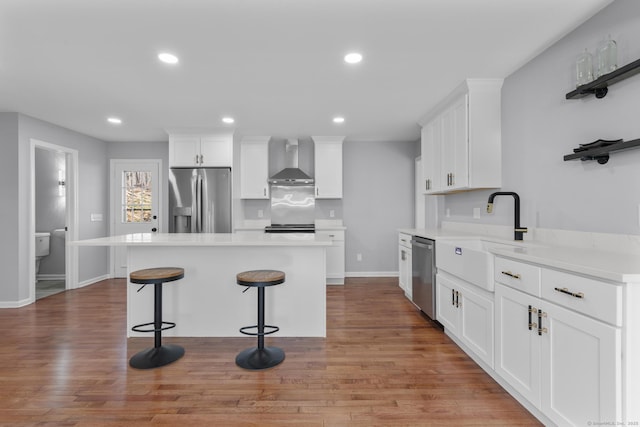 kitchen with wall chimney exhaust hood, appliances with stainless steel finishes, a kitchen bar, white cabinetry, and a sink