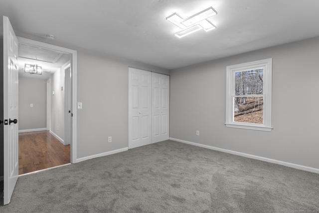 unfurnished bedroom with attic access, a closet, carpet flooring, and baseboards