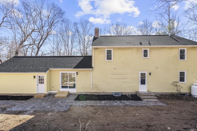 rear view of property featuring a shingled roof, entry steps, a patio, and a chimney