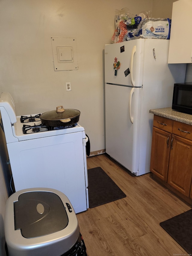 kitchen with white appliances, electric panel, and light wood-type flooring