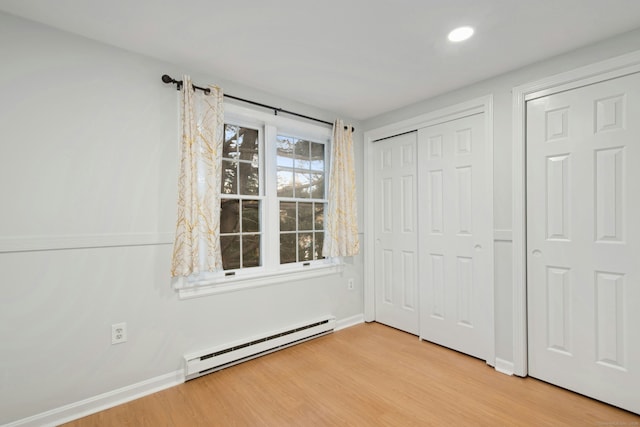 unfurnished bedroom with a baseboard heating unit, light hardwood / wood-style floors, and a closet