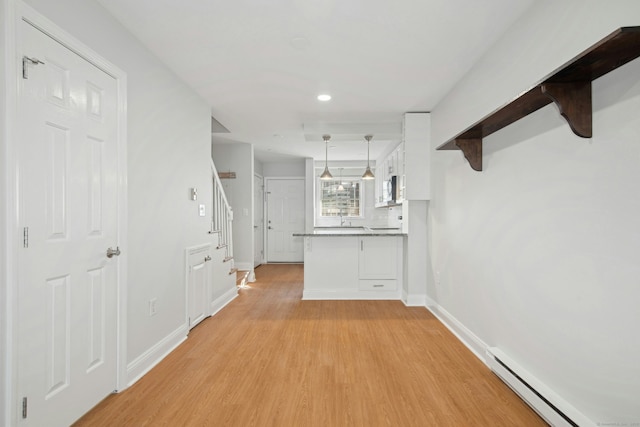 hallway with a baseboard heating unit, light hardwood / wood-style floors, and sink