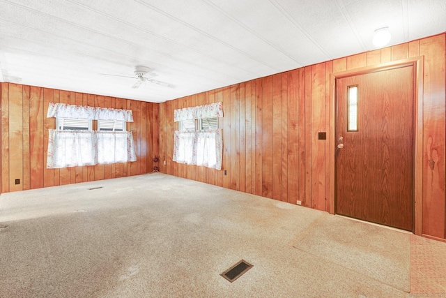 foyer with ceiling fan, carpet, and wooden walls