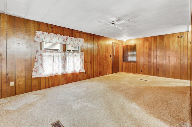 carpeted spare room featuring wooden walls and ceiling fan