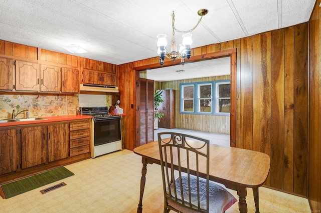 kitchen with pendant lighting, sink, a notable chandelier, gas range, and wood walls