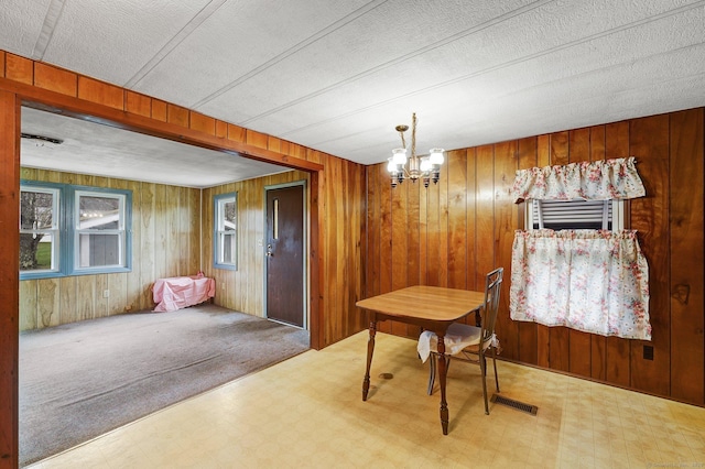 dining space featuring a textured ceiling, a notable chandelier, and wooden walls