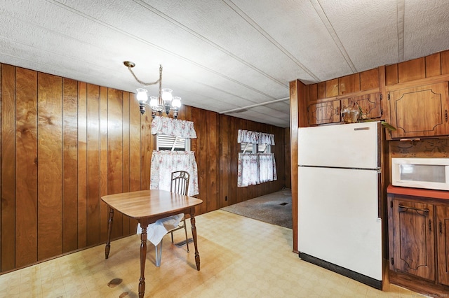 kitchen with wood walls, a chandelier, hanging light fixtures, white appliances, and a textured ceiling