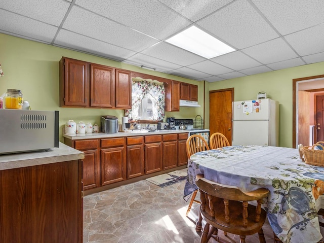 kitchen featuring a paneled ceiling, light countertops, electric range oven, freestanding refrigerator, and under cabinet range hood