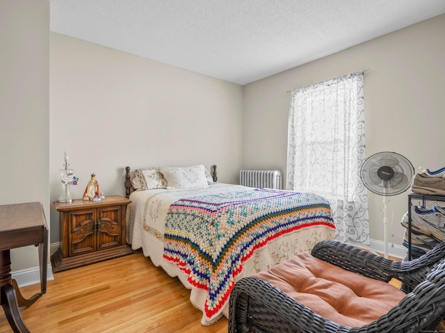 bedroom with a textured ceiling, baseboards, wood finished floors, and radiator