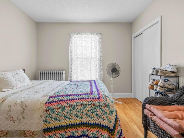 bedroom with baseboards, radiator, wood finished floors, a textured ceiling, and a closet