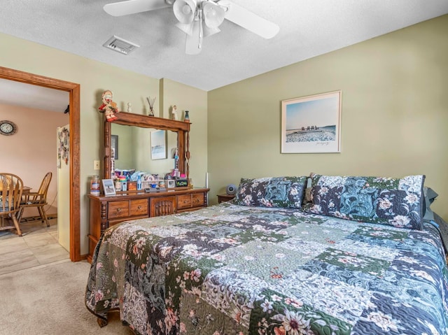 bedroom featuring a ceiling fan, light colored carpet, visible vents, and a textured ceiling