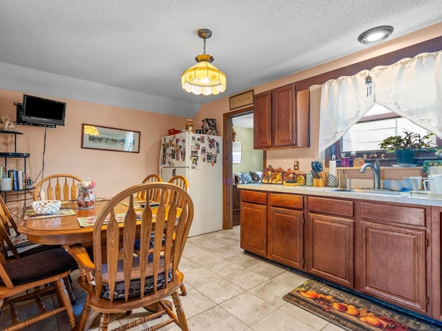 kitchen featuring brown cabinetry, freestanding refrigerator, light countertops, pendant lighting, and a sink