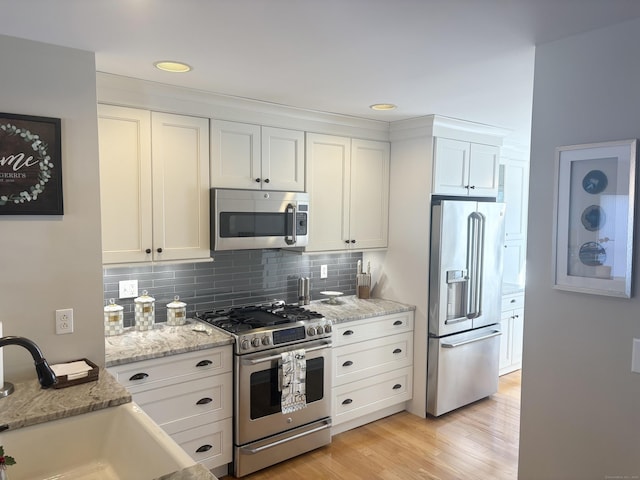 kitchen with stainless steel appliances, light stone countertops, sink, and white cabinets