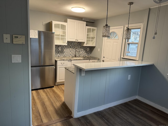 kitchen featuring stainless steel refrigerator, white cabinets, dark hardwood / wood-style flooring, hanging light fixtures, and kitchen peninsula