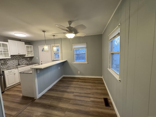 kitchen with dark hardwood / wood-style floors, tasteful backsplash, white cabinets, hanging light fixtures, and kitchen peninsula