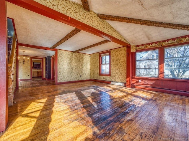 unfurnished living room featuring an inviting chandelier, hardwood / wood-style flooring, lofted ceiling with beams, and a textured ceiling