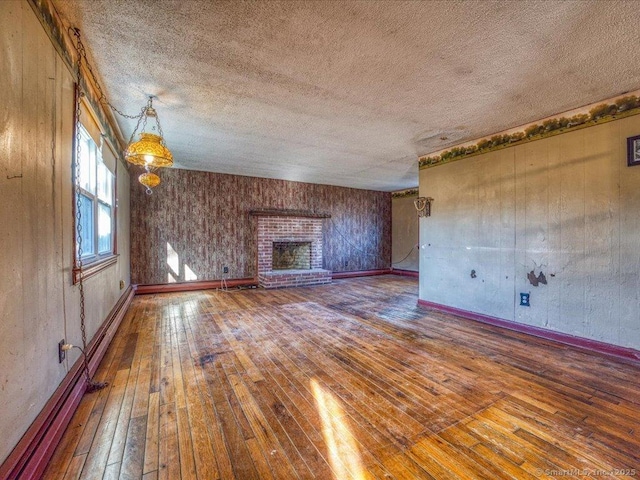 unfurnished living room featuring wood-type flooring, a textured ceiling, a brick fireplace, and a baseboard heating unit