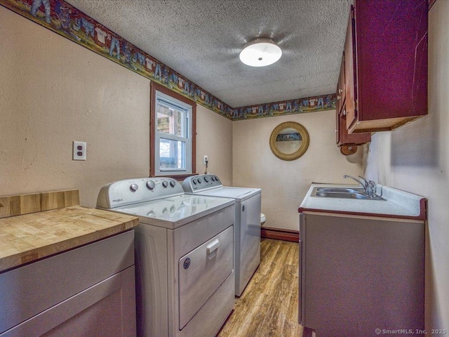 washroom with sink, cabinets, washing machine and clothes dryer, light hardwood / wood-style floors, and a textured ceiling