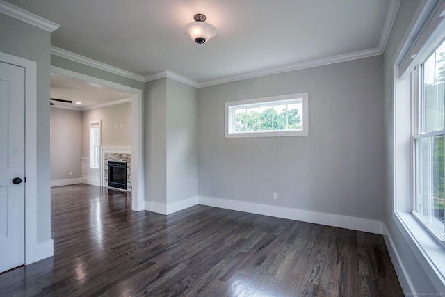 empty room featuring crown molding, baseboards, dark wood-type flooring, and a stone fireplace