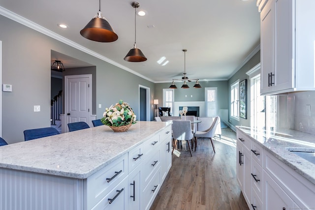 kitchen with decorative light fixtures, a fireplace, white cabinetry, and a center island