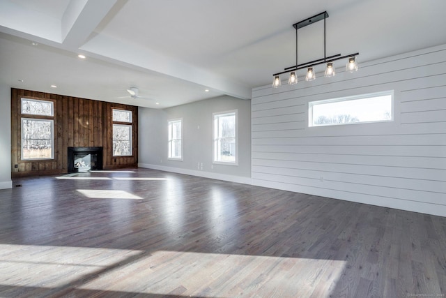 unfurnished living room with dark hardwood / wood-style flooring, beam ceiling, wooden walls, and a healthy amount of sunlight