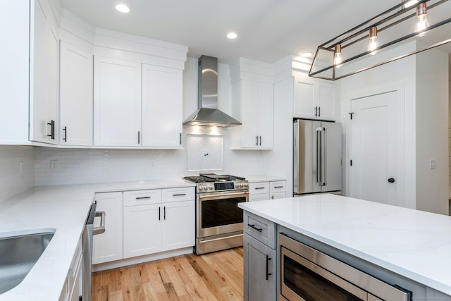 kitchen featuring wall chimney exhaust hood, light stone counters, pendant lighting, stainless steel appliances, and white cabinets