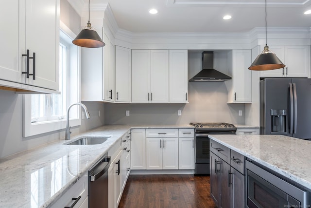 kitchen with wall chimney range hood, sink, appliances with stainless steel finishes, hanging light fixtures, and white cabinets