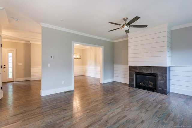 unfurnished living room featuring a tiled fireplace, ornamental molding, dark hardwood / wood-style floors, and ceiling fan