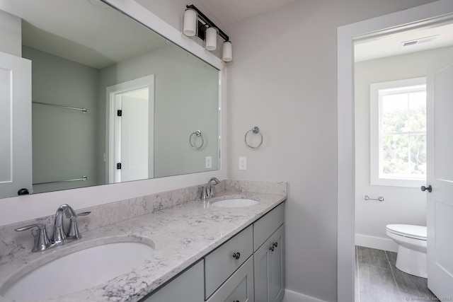 full bath featuring double vanity, a sink, toilet, and baseboards