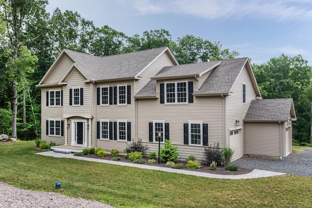 colonial inspired home featuring a garage, roof with shingles, a front yard, and gravel driveway