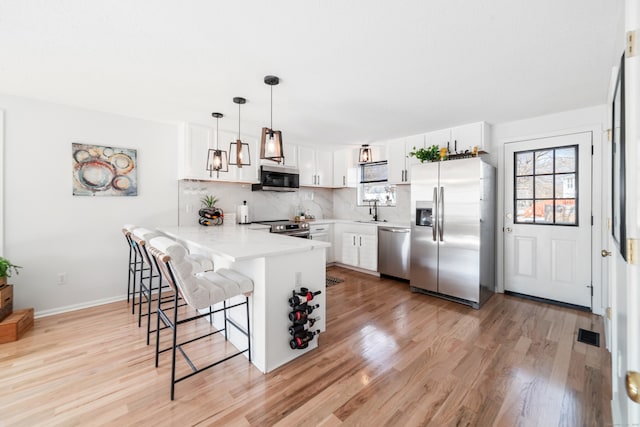 kitchen featuring appliances with stainless steel finishes, decorative light fixtures, tasteful backsplash, white cabinetry, and a kitchen breakfast bar