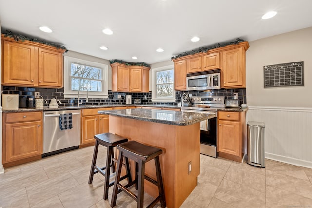 kitchen with appliances with stainless steel finishes, sink, a breakfast bar area, dark stone countertops, and a center island