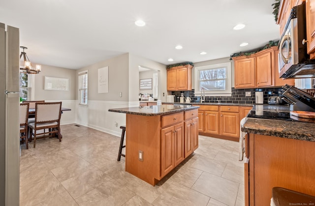 kitchen featuring a breakfast bar, sink, a center island, hanging light fixtures, and dark stone countertops