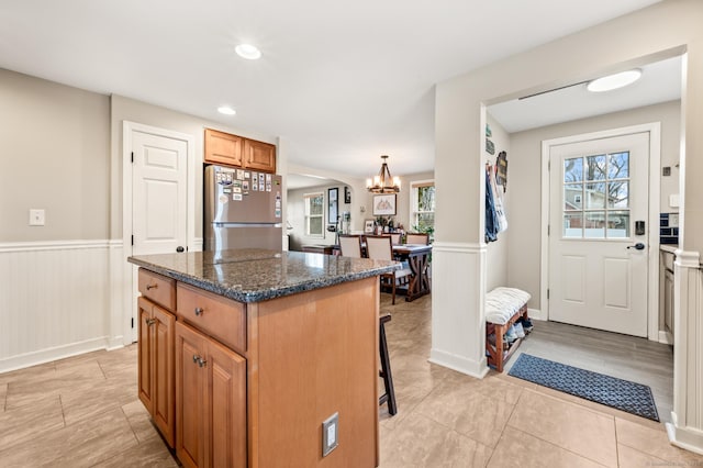 kitchen with a breakfast bar, stainless steel refrigerator, a center island, decorative light fixtures, and dark stone counters