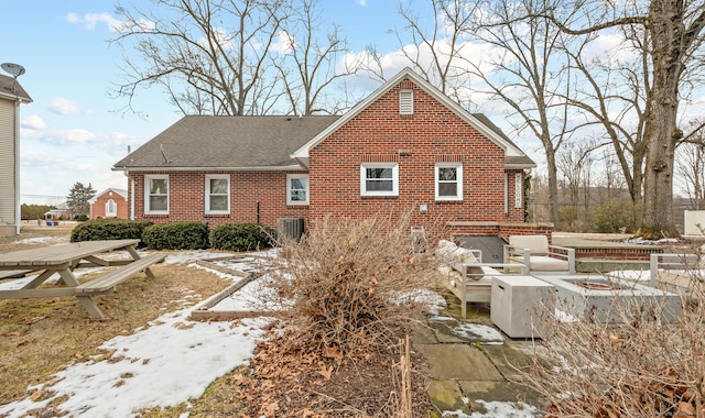 snow covered back of property featuring central AC unit and a fire pit