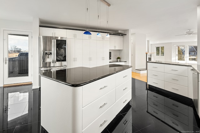 kitchen featuring decorative light fixtures, white cabinetry, stainless steel fridge, a center island, and a healthy amount of sunlight