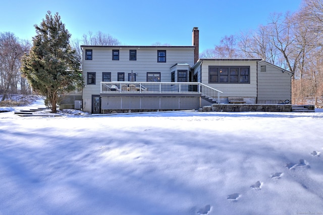 snow covered back of property with cooling unit and a wooden deck