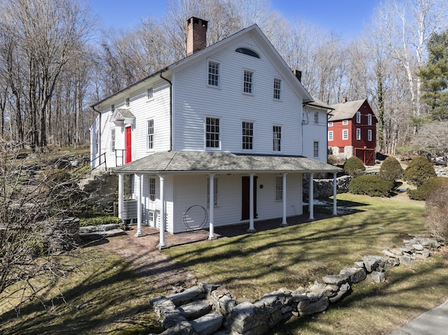 rear view of property featuring central air condition unit, covered porch, a chimney, and a lawn