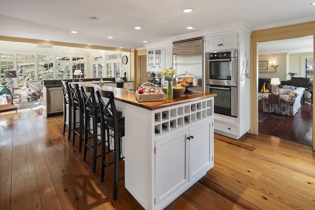 kitchen with a kitchen island, ornamental molding, butcher block countertops, dark wood-type flooring, and stainless steel appliances