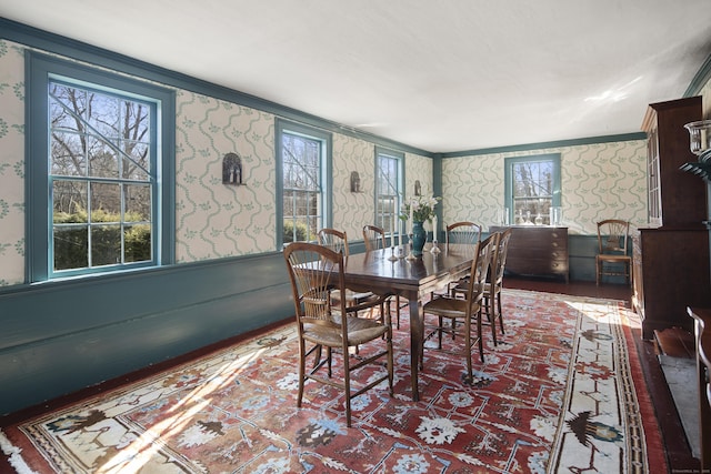 dining area with ornamental molding, wood finished floors, wainscoting, and wallpapered walls