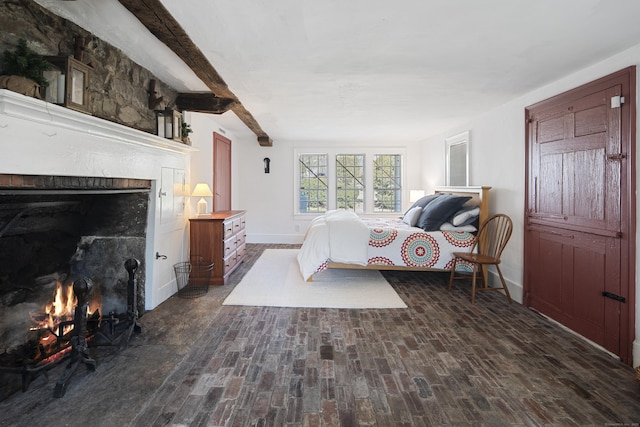 bedroom with brick floor, a lit fireplace, baseboards, and beam ceiling