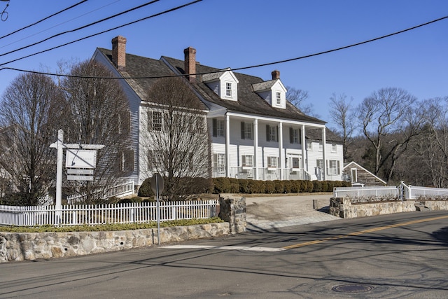 cape cod home with covered porch, a fenced front yard, and a chimney